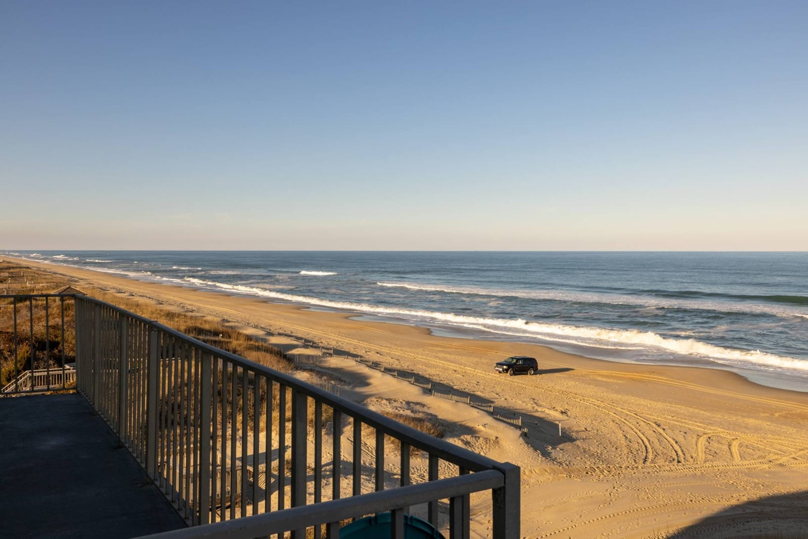The Atlantic from the top-floor balcony, the railing in the foreground and open beach curving into the distance.